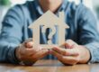Concept per domanda tra comprare casa o affittarla: persona con modellino di abitazione in mano con punto di domanda