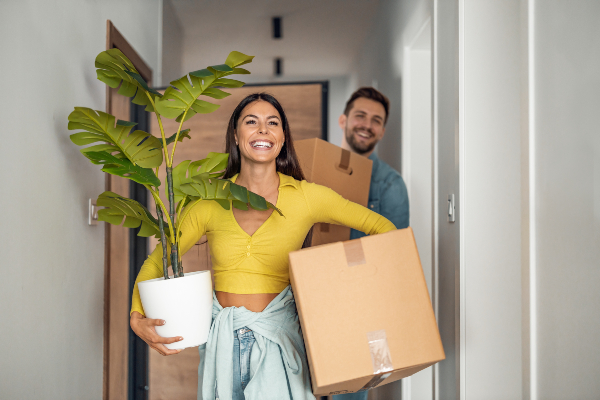 Concept per investire in una seconda casa: coppia sorridente entra in casa con una pianta e scatoloni - Replanner